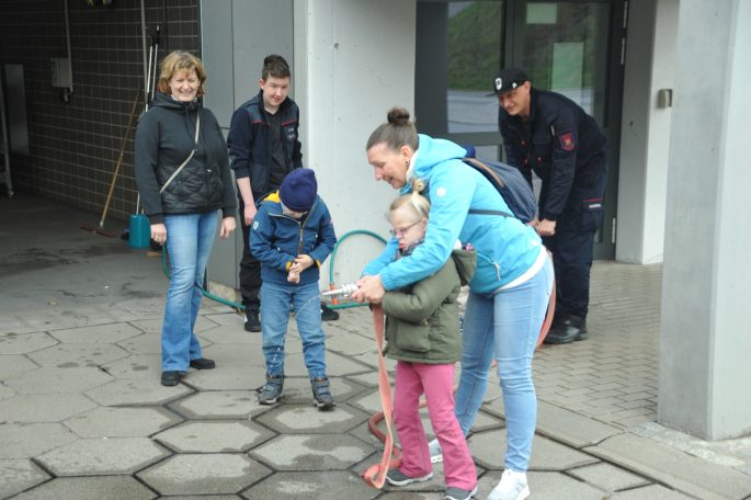 Eine Gruppe von Personen, darunter Kinder, spielt mit einem Schlauch vor einem Gebäude.