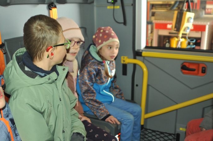 Drei Kinder sitzen in einem Fahrzeug und schauen neugierig nach draußen.