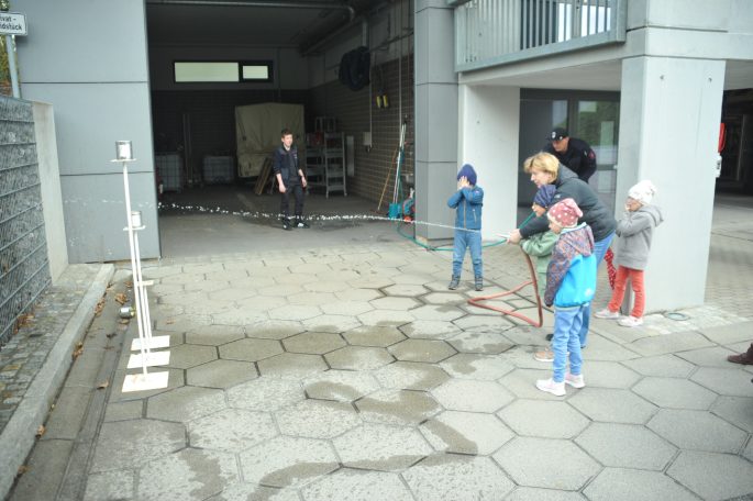 Kinder stehen auf einem Gehweg und beobachten eine Wasseraktion im Freien.